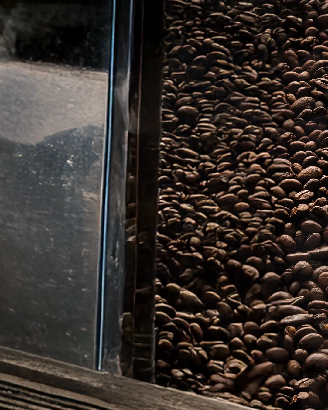 Vista ravvicinata di un contenitore di vetro pieno di chicchi di caffè tostati, con la luce che si riflette sulla superficie di vetro sul lato sinistro dell'immagine.