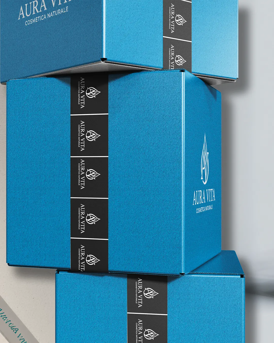 Tre scatole blu con il logo e il testo AURA VITA COSMETICA NATURALE impilate l'una sull'altra, sigillate con nastro nero stampato con lo stesso logo e marchio.