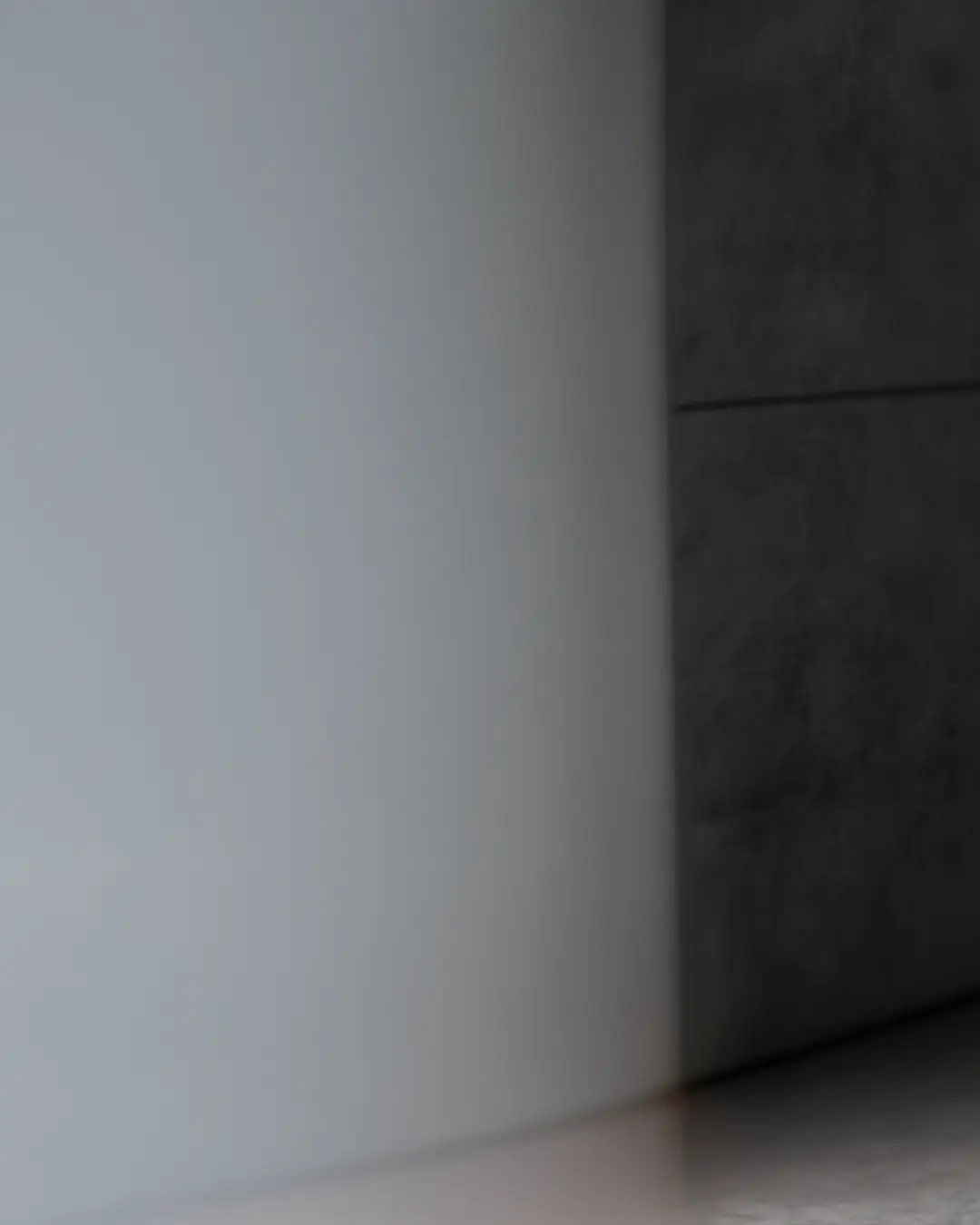 Una scena minimalista che mostra il bordo curvo di una parete liscia di colore grigio chiaro che incontra una parete di colore grigio più scuro con giunture orizzontali. L'illuminazione crea ombre e sfumature sottili sulle superfici.