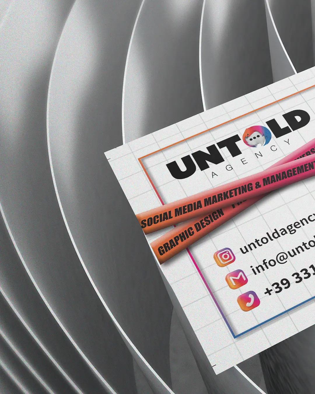 Primo piano di due biglietti da visita della Untold Agency su una superficie dalle linee curve e argentate. I biglietti da visita riportano il logo dell'agenzia, i dati di contatto e le icone di Instagram, e-mail e numero di telefono.