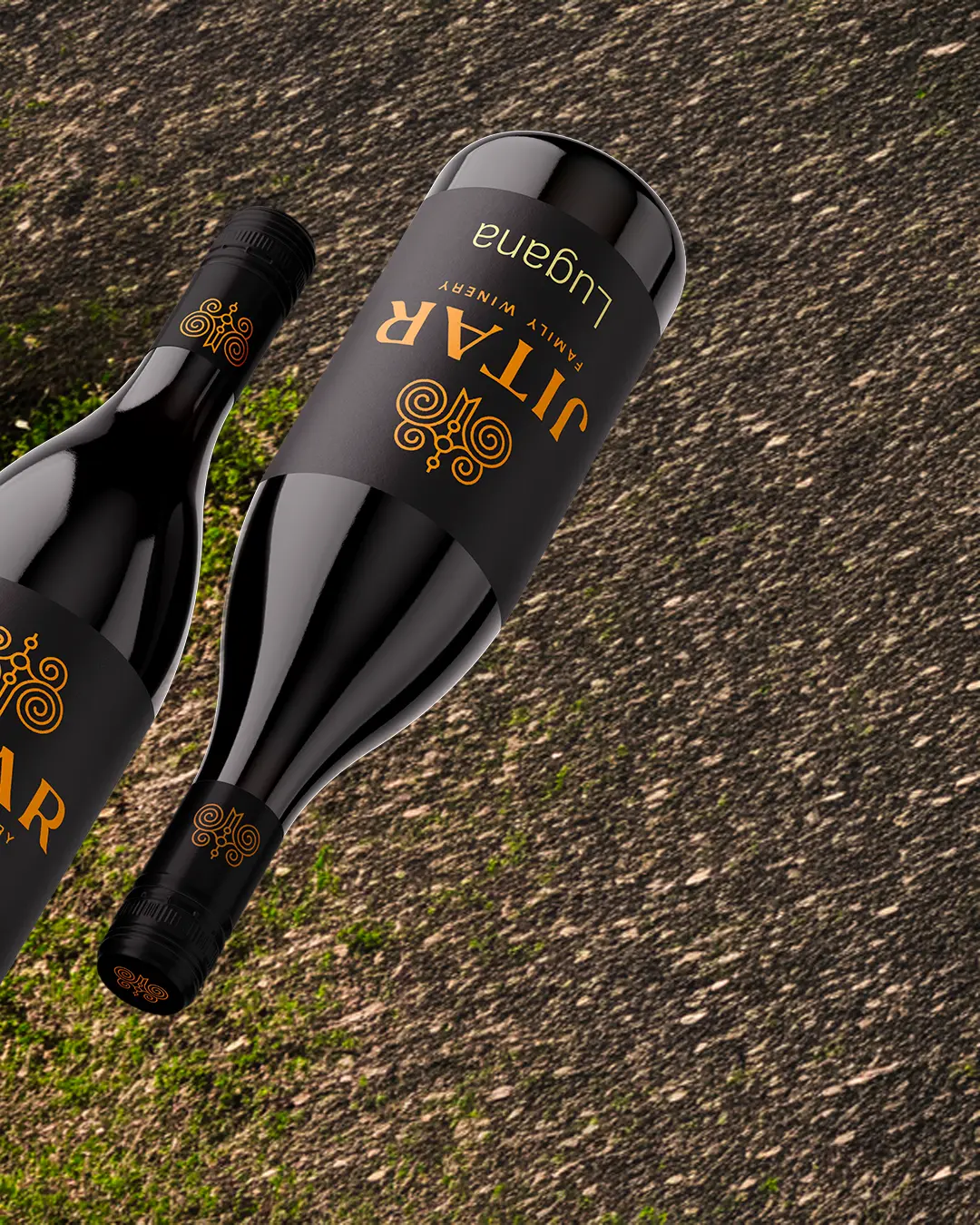 Due bottiglie di vino nere con etichette dorate e arancioni della JITAR Family Winery Lugana giacciono su una superficie strutturata con macchie di erba verde. Le bottiglie sono posizionate in diagonale con le etichette ben visibili.