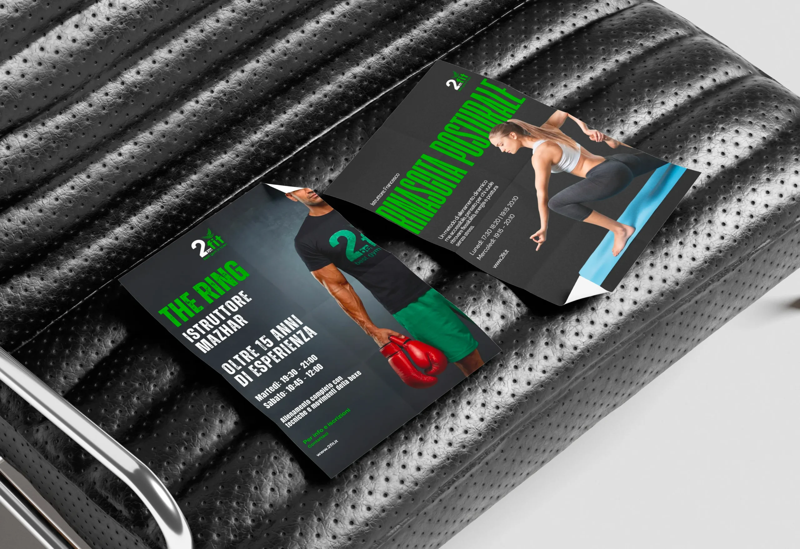 Due volantini di fitness in italiano sono appoggiati su una sedia in pelle nera traforata. Un volantino raffigura un uomo con guantoni da boxe rossi, mentre l'altro mostra una donna che esegue un esercizio di push-up.